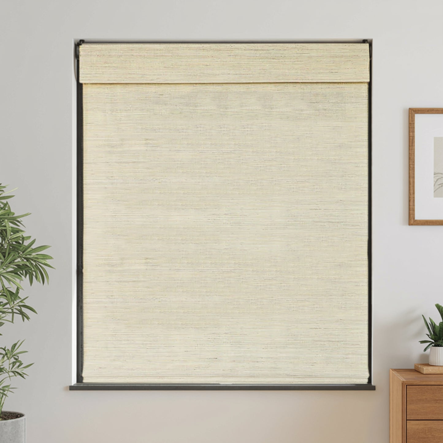 Beige woven blind in a room with a plant and a dresser.